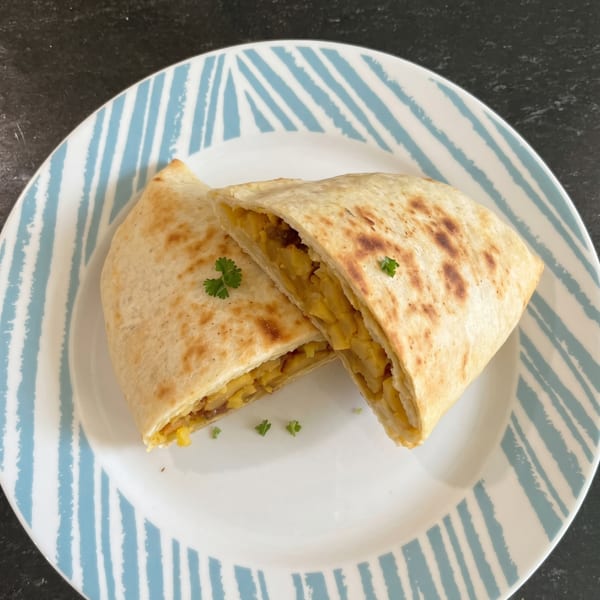 Two golden-brown quesadilla halves, filled with yellow corn and potatoes, garnished with parsley on a striped plate.