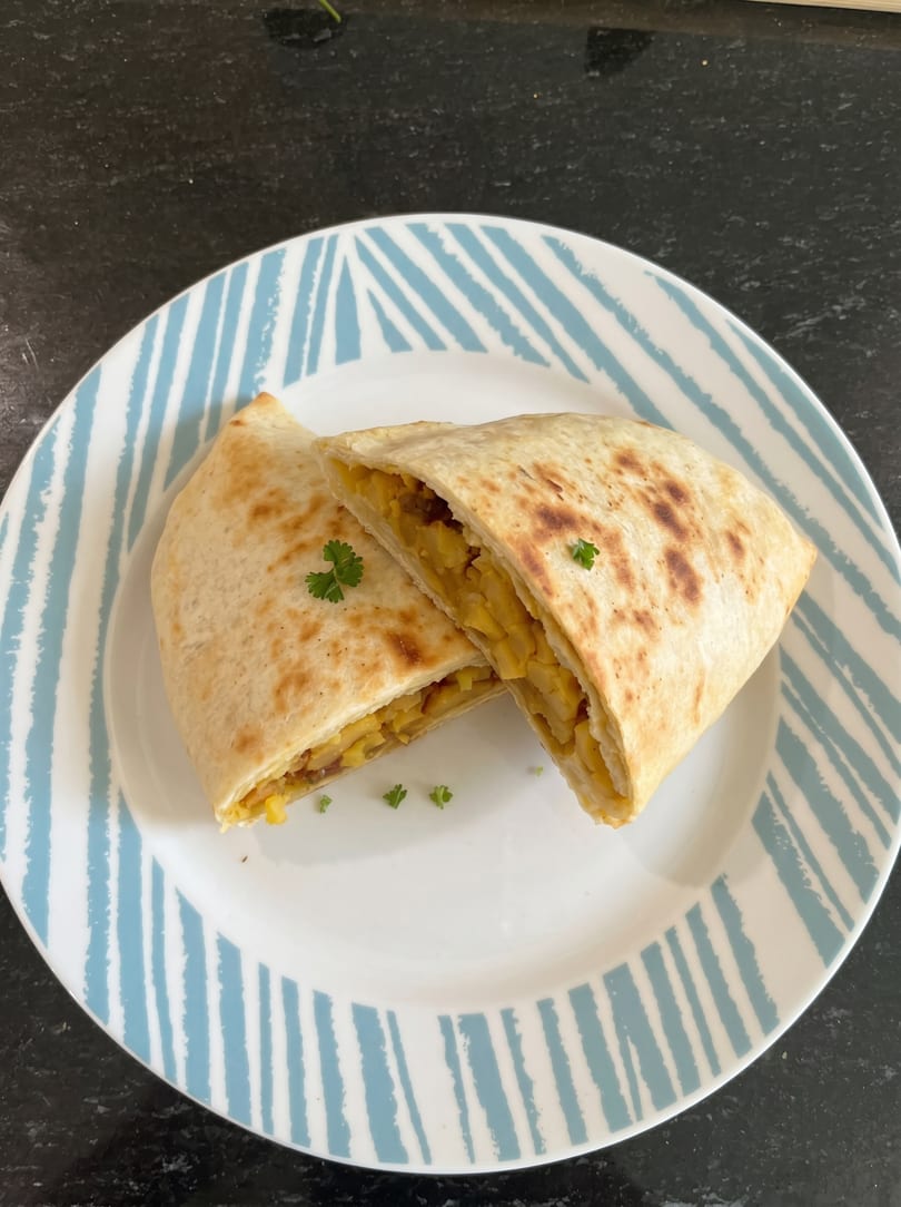 Two golden-brown quesadilla halves, filled with yellow corn and potatoes, garnished with parsley on a striped plate.