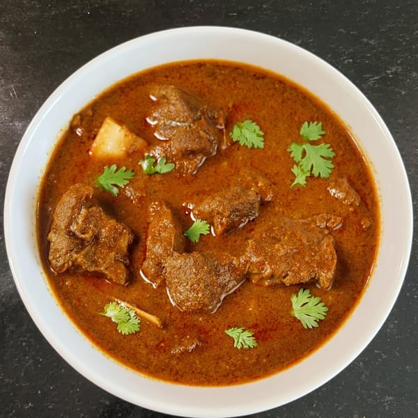 A white bowl filled with rich, reddish-brown curry, garnished with fresh green cilantro leaves.