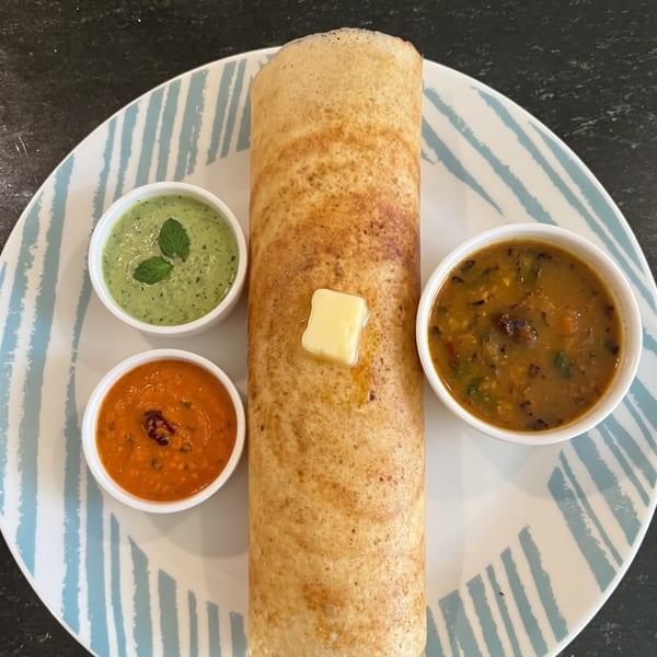 Rolled dosa with a pat of butter, served with green chutney, red chutney, and sambar.