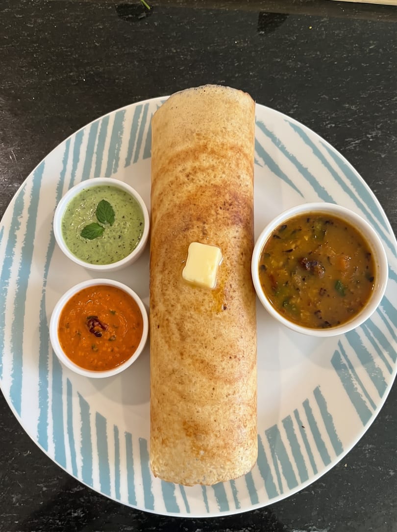 Rolled dosa with a pat of butter, served with green chutney, red chutney, and sambar.