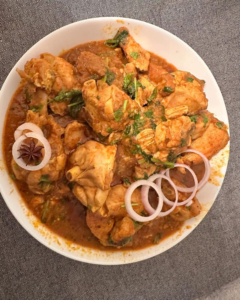 Chicken curry with cilantro, star anise, and red onion slices in a white bowl.